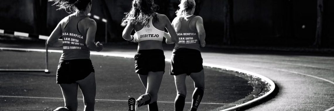 Black and white back view of unrecognizable fit female runners in sportswear running during track and field competition